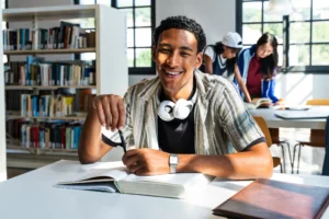 Chico en biblioteca estudiando y sonriendo